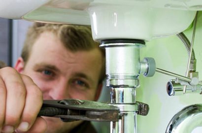 Plumber using a wrench to tighten a siphon under a sink.